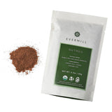 A green and white Evermill branded package labeled "Organic Nutmeg Refill" alongside a small pile of ground spice. The package details include tasting notes (pungent, nutty, warm), suggested complements (candied nuts, eggnog, shepherd's pie), and a net weight of 2.3 oz (66g). Derived from the South Asian Nutmeg Tree.