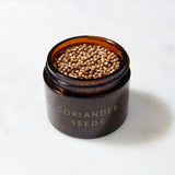 An Evermill jar labeled "Organic Coriander Seeds Refill" is filled with small, round coriander seeds, renowned for their distinct flavor profile. The brown glass jar rests on a smooth, white surface, ready to enhance dishes with a touch of Bulgaria's culinary heritage.