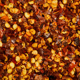 A close-up view of a colorful spice collection, featuring Evermill's Organic Red Pepper Flakes Refill, seeds, and various dried vegetables. The blend creates a vibrant and textured pattern, showcasing the diverse ingredients used in culinary seasoning with a touch of savory heat.