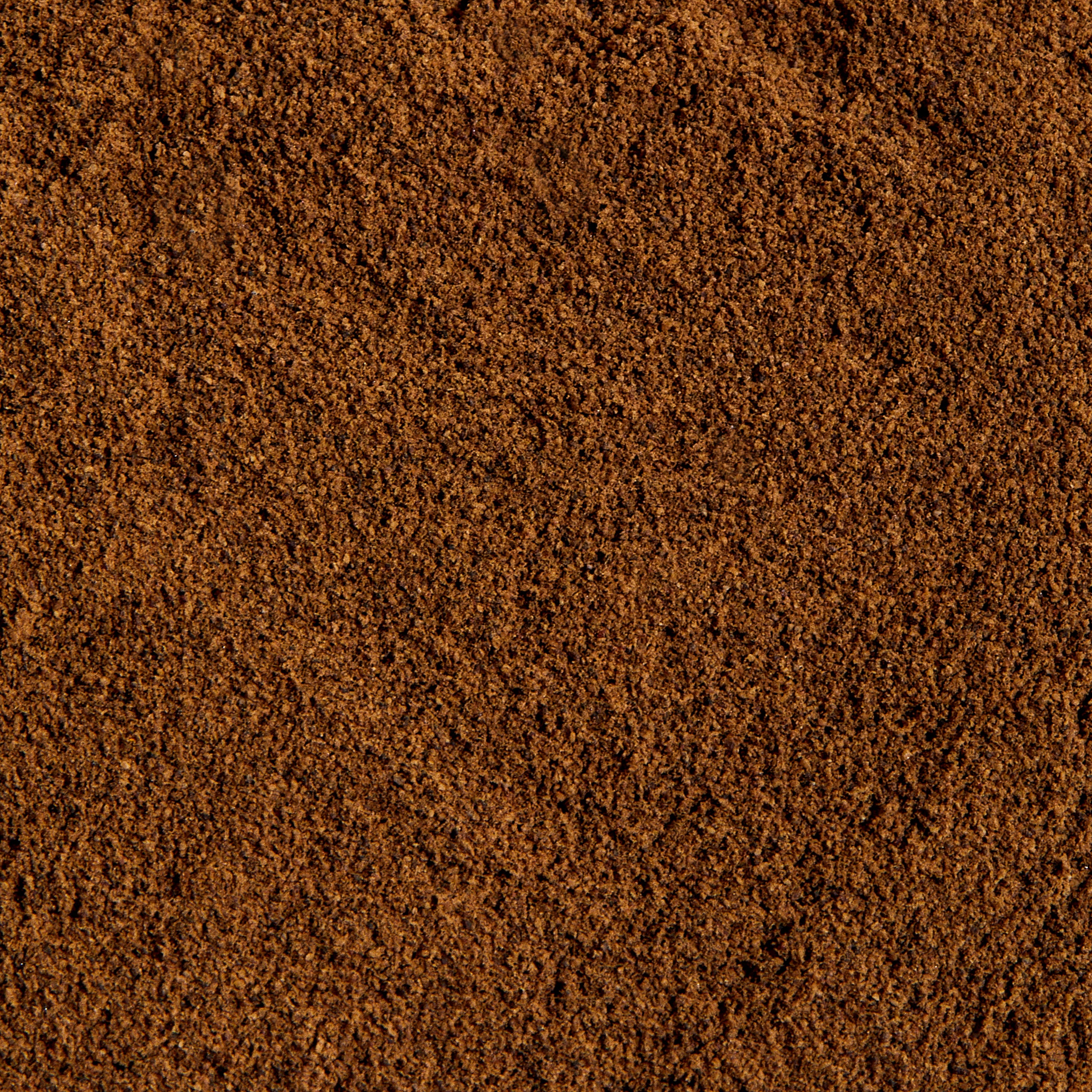 Close-up of a surface covered with finely ground Organic Allspice Refill by Evermill, showing a uniform, dark brown textured appearance reminiscent of dried berries.